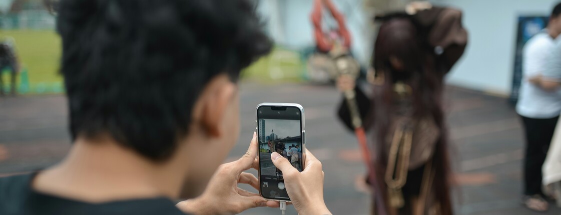 Freizeitgestaltung in Innsbruck Eine Jugendlicher mit schwarzem T-Shirt fotografiert mit seinem Handy einen Cosplay-Charakter.