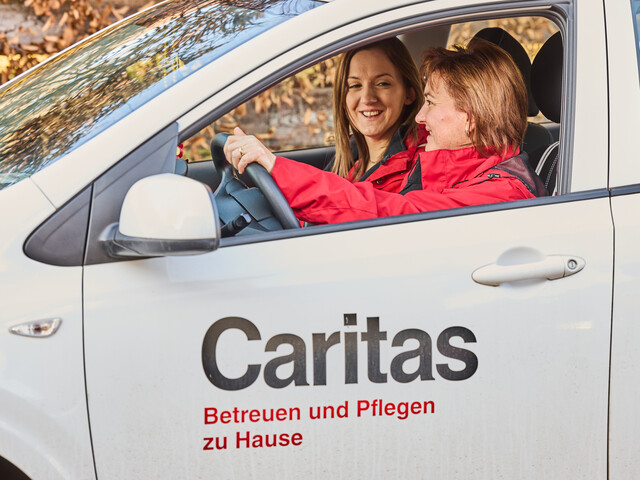 Pflegefachkraft und Praktikantin sitzen gemeinsam im Dienstauto.