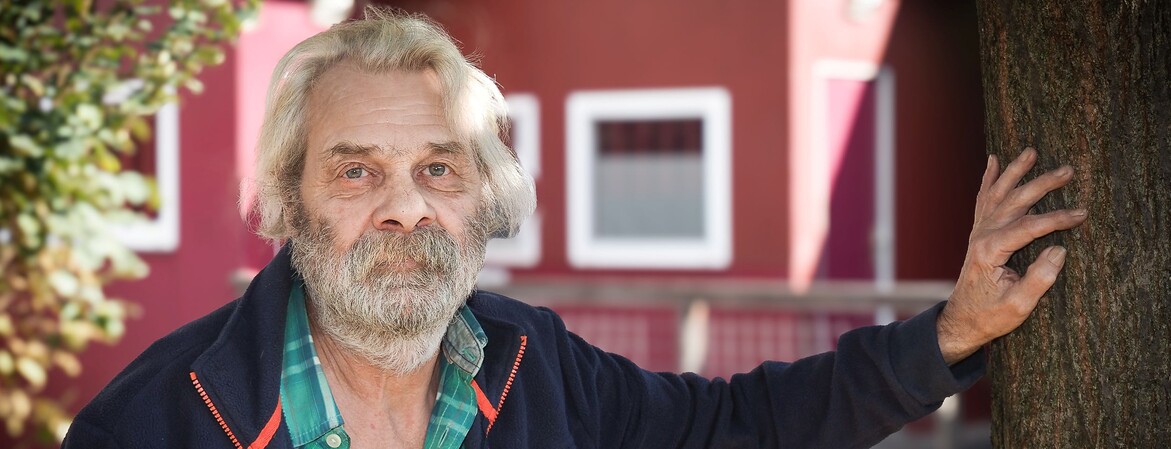 Bewohner des Ressidorfs stützt sich mit der Hand an einem Baum ab