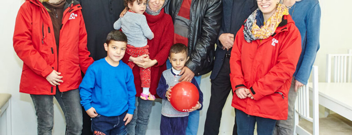 Drei Caritas-Mitarbeiterinnen, der Direktor der Caritas St. Pölten und ein Geistlicher mit einer Flüchtlingsfamilie im Containerdorf in Melk