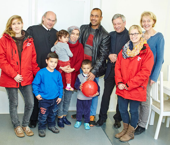 Drei Caritas-Mitarbeiterinnen, der Direktor der Caritas St. Pölten und ein Geistlicher mit einer Flüchtlingsfamilie im Containerdorf in Melk