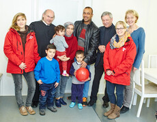 Drei Caritas-Mitarbeiterinnen, der Direktor der Caritas St. Pölten und ein Geistlicher mit einer Flüchtlingsfamilie im Containerdorf in Melk