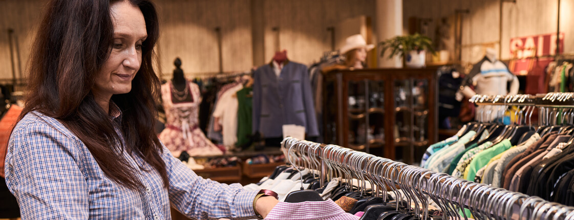 Frau hängt Gewand in einem Carla Shop (Second Hand Shop) auf