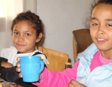 Zwei Mädchen im Kinderzentrum Eden, eines hält eine blaue Tasse, beide wirken entspannt und zufrieden.