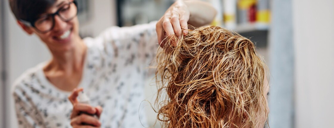 Eine Friseurin besprüht die Haare einer Kundin mit Pflegeprodukt