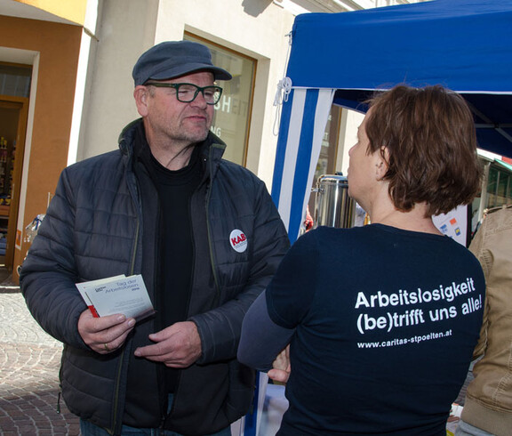 Tag der Arbeitslosen - eine Caritas Mitarbeiterin spricht mit einem Interessierten