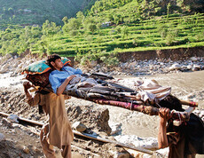 in Pakistan wird ein Verletzter auf einer Trage von zwei Anderen getragen