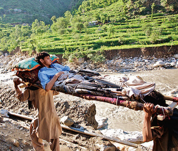 in Pakistan wird ein Verletzter auf einer Trage von zwei Anderen getragen
