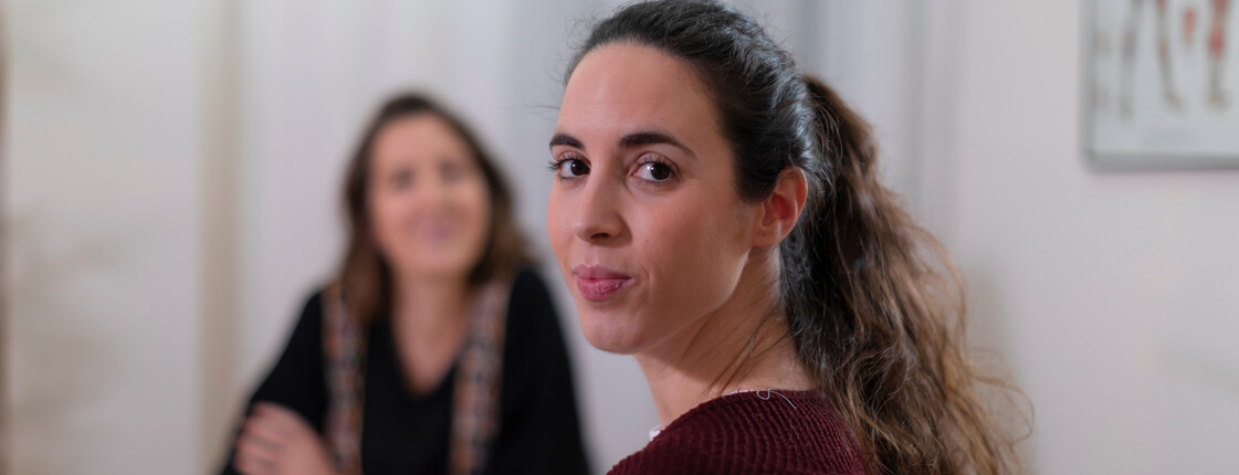 Integrationsprojekt Tiroler Patin Portrait einer Frau mit dunklen Haaren, die über ihre Schulter in die Kamera schaut während sie sich in einem Beratungsgespräch befindet.