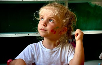 Blondes Mädchen mit Kirschmotiv auf der Wange nimmt am Kinderprogramm in Puka, Albanien, teil