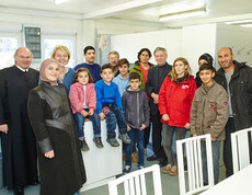 Caritas-Mitarbeiter mit einer Flüchtlingsfamilie und einem Geistlichen im Containerdorf in Melk