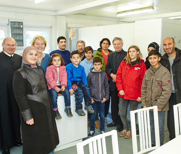 Caritas-Mitarbeiter mit einer Flüchtlingsfamilie und einem Geistlichen im Containerdorf in Melk