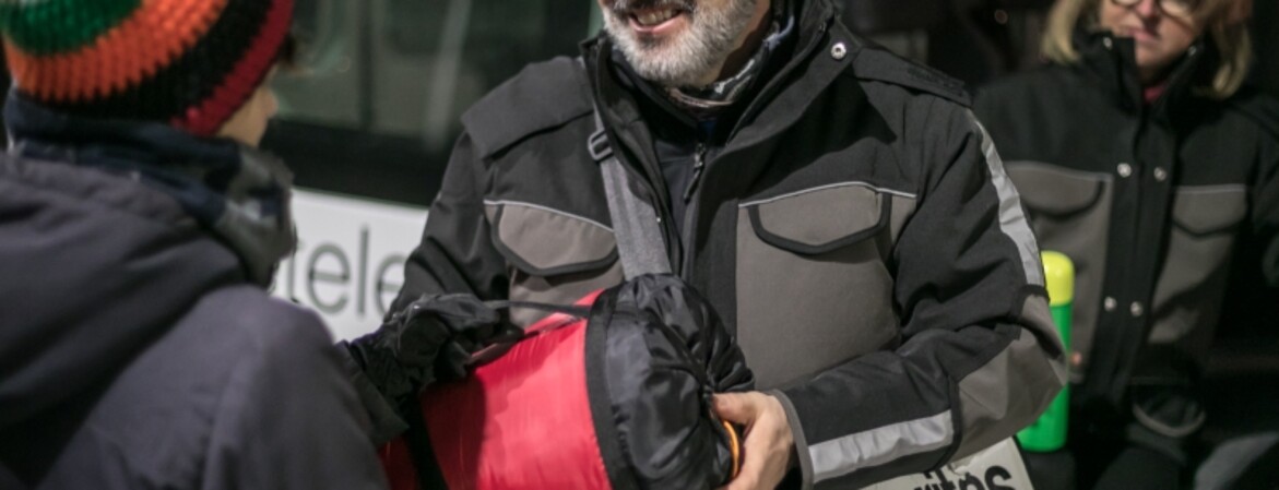 Ein Mann übergibt einer Person einen Schlafsack