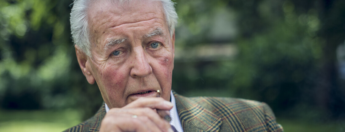 Caritas Angehörigenarbeit Portrait eines älteren Herrn, der in einem Garten sitzt und raucht.