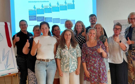 Gruppe von Personen gibt Daumen hoch vor Präsentationstafel