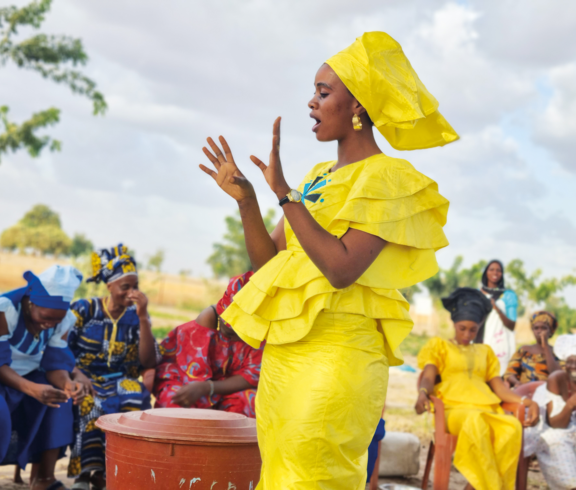 Eine Frau in gelber traditioneller Kleidung spricht vor einer Gruppe von Frauen in Burkina Faso.