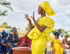 Eine Frau in gelber traditioneller Kleidung spricht vor einer Gruppe von Frauen in Burkina Faso.