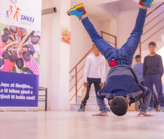 Ein Junge macht eine akrobatische Bewegung auf den Händen, während andere Kinder im Haus Eden Straßenkinderzentrum in Tirana zusehen.