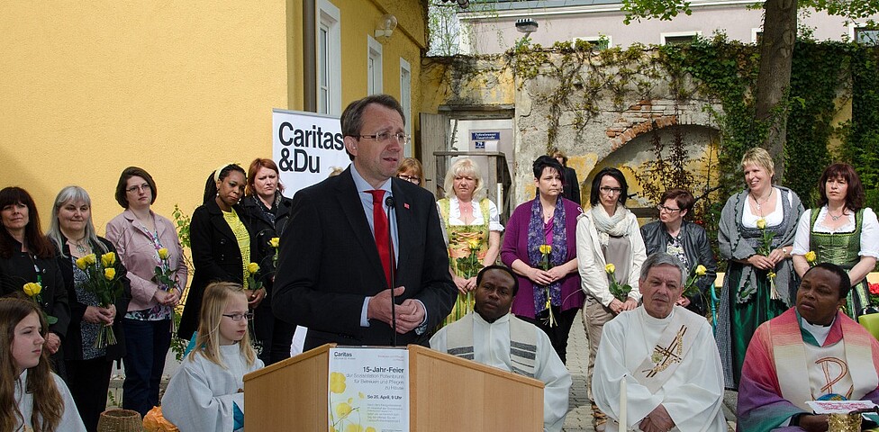 Bürgermeister von St. Pölten spricht ins Mikrofon und hinter ihm stehen Frauen mit gelben Rosen