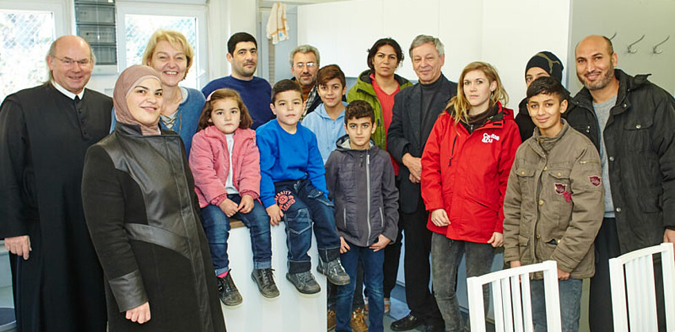 Caritas-Mitarbeiter mit einer Flüchtlingsfamilie und einem Geistlichen im Containerdorf in Melk