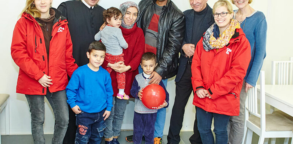 Drei Caritas-Mitarbeiterinnen, der Direktor der Caritas St. Pölten und ein Geistlicher mit einer Flüchtlingsfamilie im Containerdorf in Melk