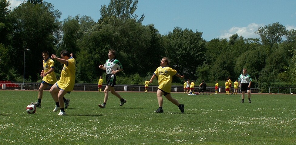 Mehrere Personen spielen in zwei Mannschaften mit verschiedenen Trikots Fußball.