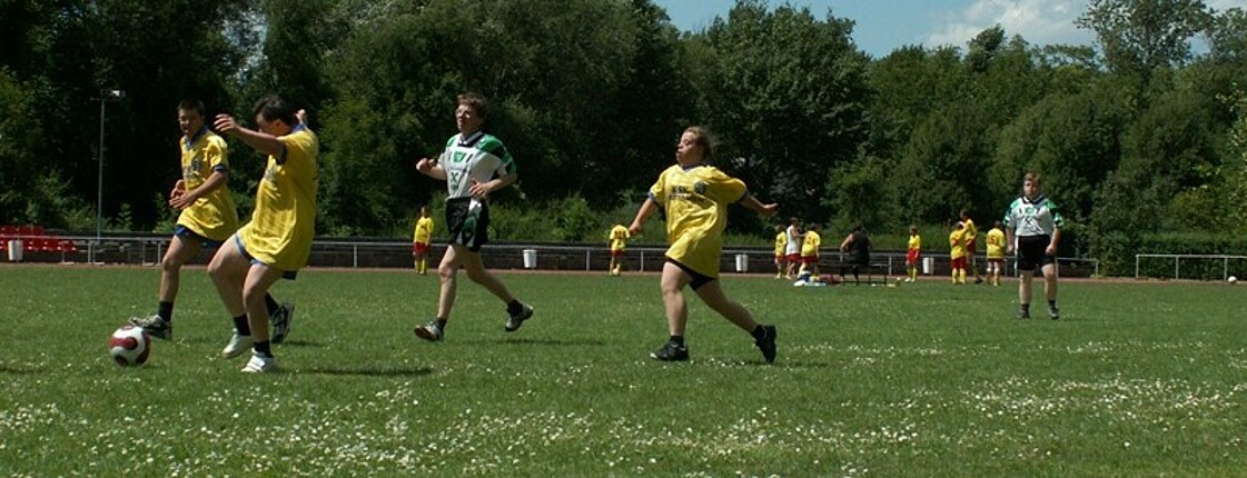 Mehrere Personen spielen in zwei Mannschaften mit verschiedenen Trikots Fußball.