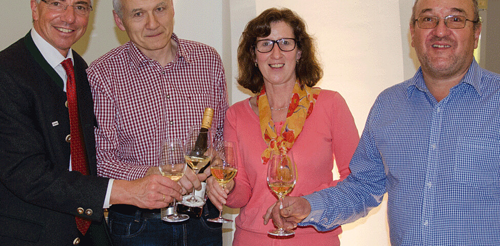Vier Personen lächeln mit einem Glas Wein in der Hand in die Kamera