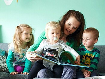 Eine Tagesmutter liest zusammen mit drei Kindern ein Buch.