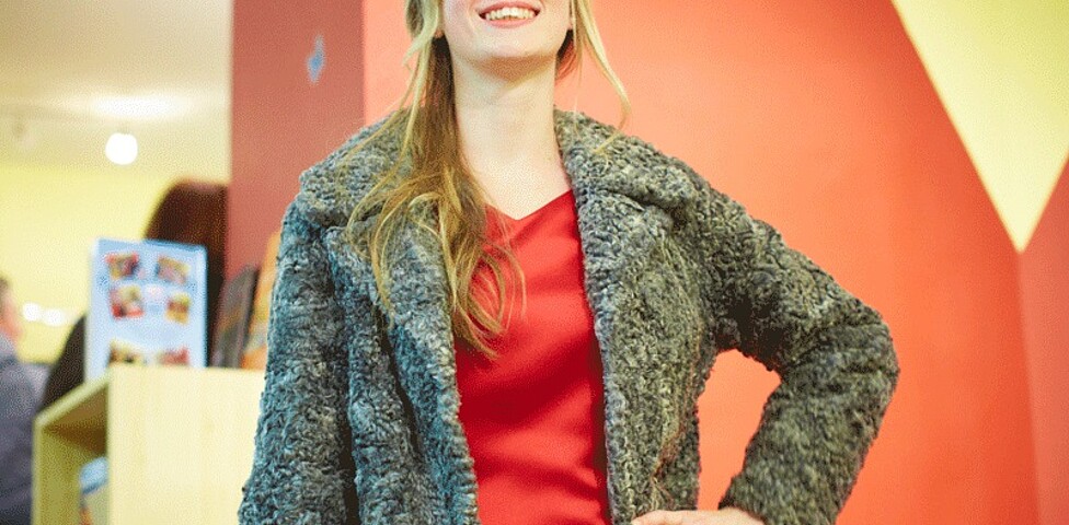 Eine Frau in einem roten Kleid und grauen Jacke der carla Amstetten