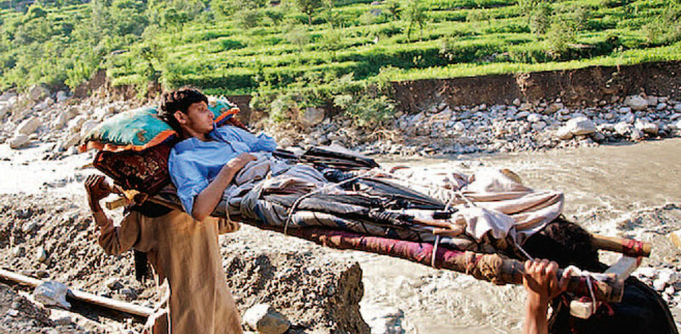 in Pakistan wird ein Verletzter auf einer Trage von zwei Anderen getragen