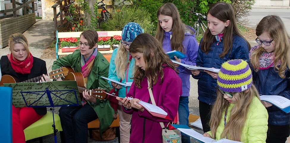 junge Mädchen singen während wie junge Frauen sie mit der Gitarre begleiten.