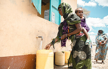 Eine Frau in afrikanischem Gewand füllt einen Kanister mit Wasser